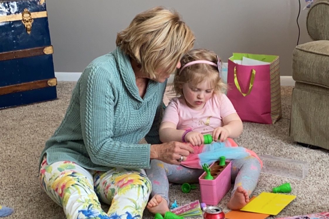 Sue sitting on the floor helping a little girl with a toy, with books nearby
